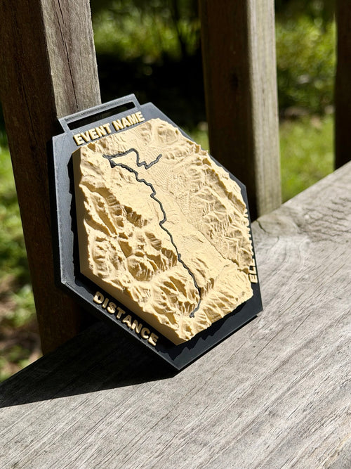 Angled view of a Race Topos 3D topographic medal showing raised terrain and lettering on a black hexagonal frame.