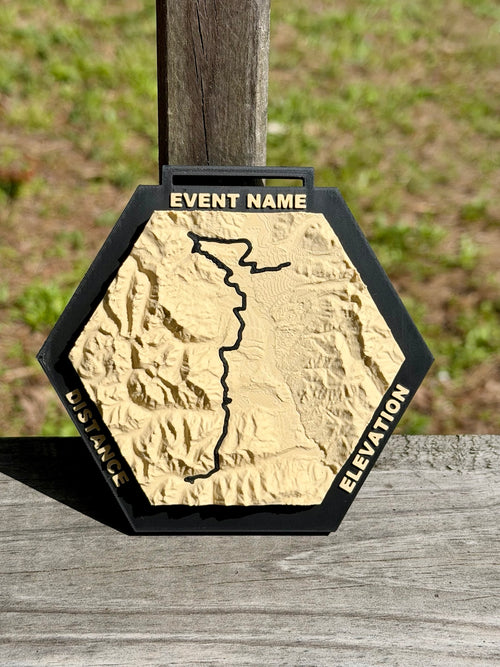 Front view of a Race Topos hexagonal 3D topographic medal with cream terrain, a black route, raised labels, and a ribbon slot.